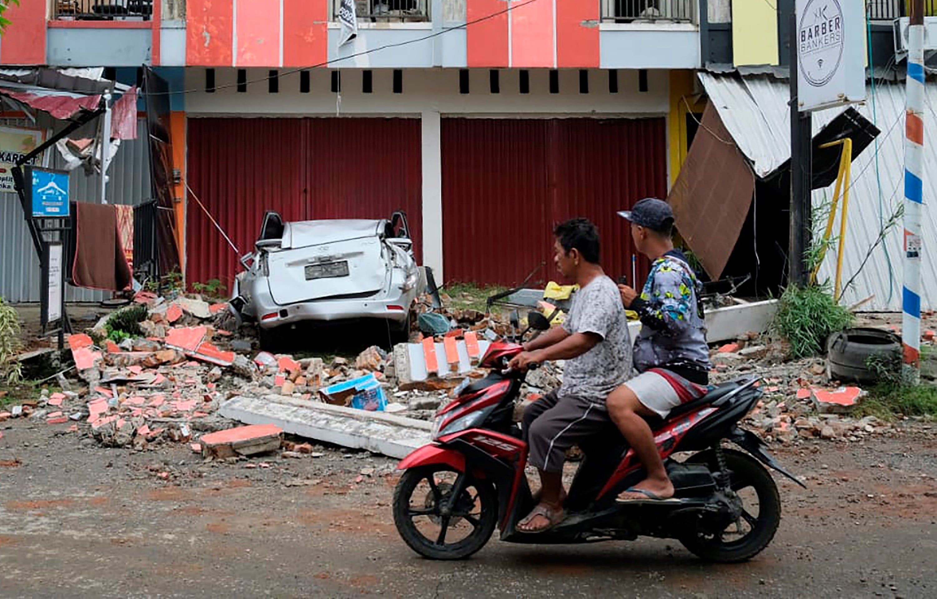 Conductor pasa junto a los restos de un automóvil dañado en un terremoto en Mamuju, West Sulawesi, Indonesia