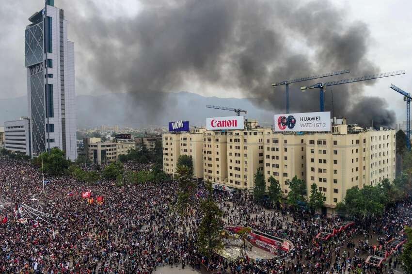 En medio de la tercera marcha masiva contra el gobierno de Piñera se podían ver las llamas del incendio en una univerisidad | AFP