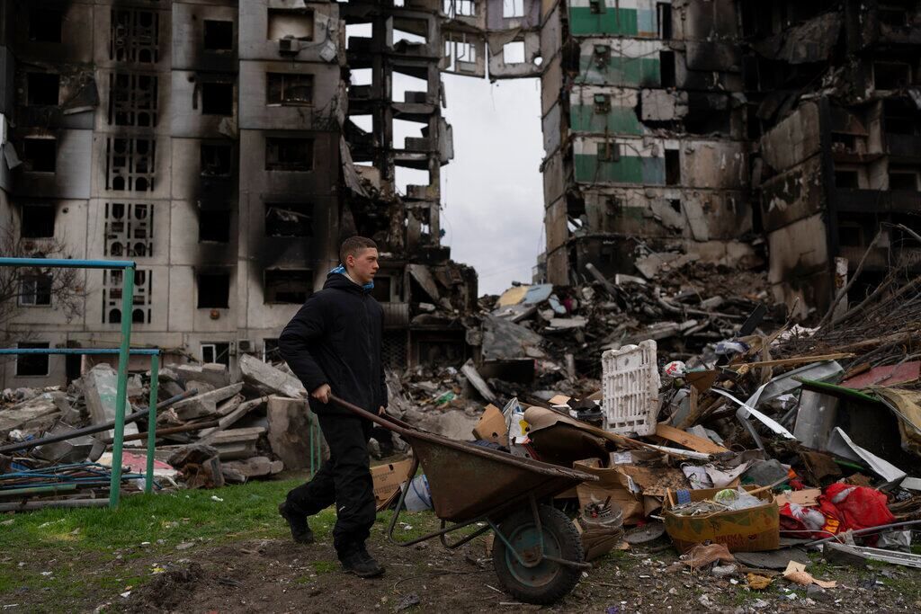 Un joven empuja una carretilla frente a un edificio residencial destruido, el domingo 10 de abril de 2022, en la localidad de Borodyanka, Ucrania. (AP)