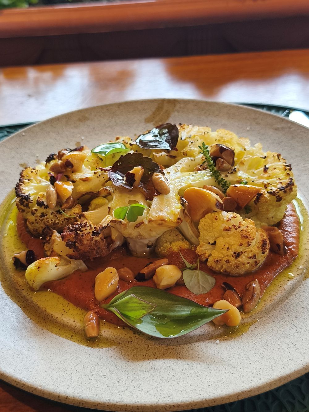 Coliflor asada sobre salsa romesco, ensalada de pancs (hierbas autóctonas alimenticias) y castañas asadas.