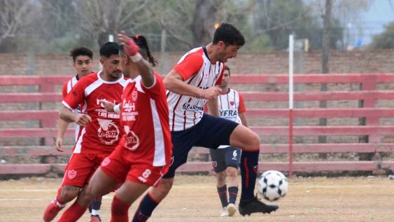 El Flaco Jesús Baldaccini se lleva el balón ante la marca de dos jugadores de Algarrobal. Talleres goleó y manda en la zona A. / Gentileza Andrés Arequipa.