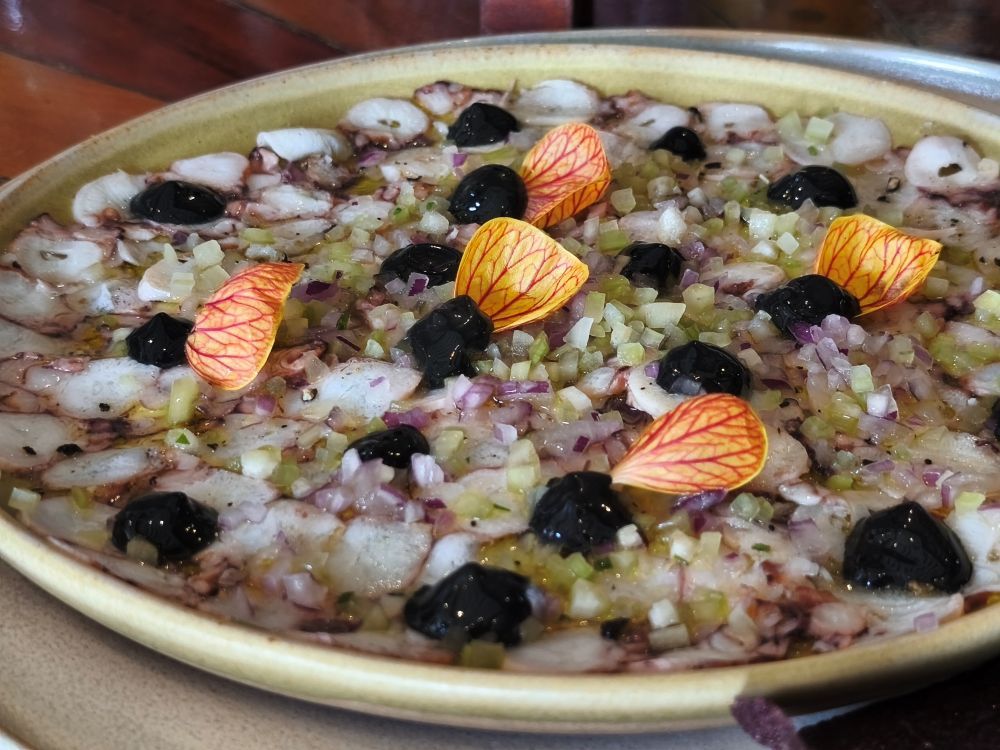 Carpaccio de pulpo con puerros, flores y otros vegetales, presentado con un notable sentido estético.