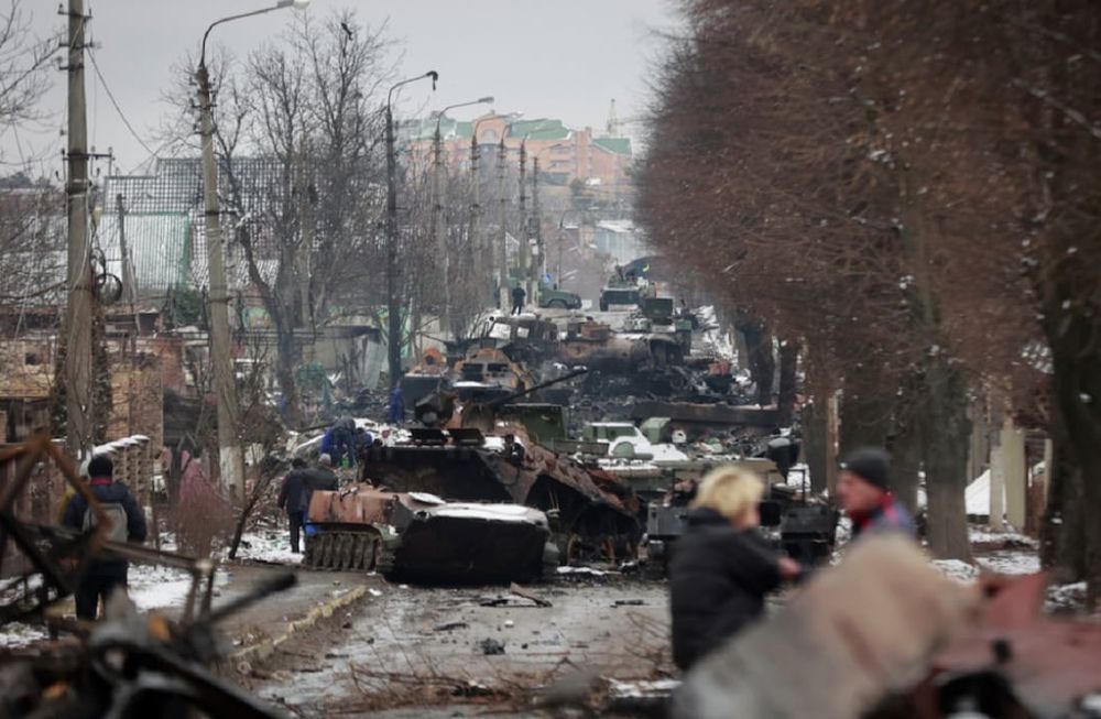 La gente mira los restos destripados de vehículos militares rusos en una carretera en la ciudad de Bucha, cerca de la capital, Kiev, Ucrania (AP)