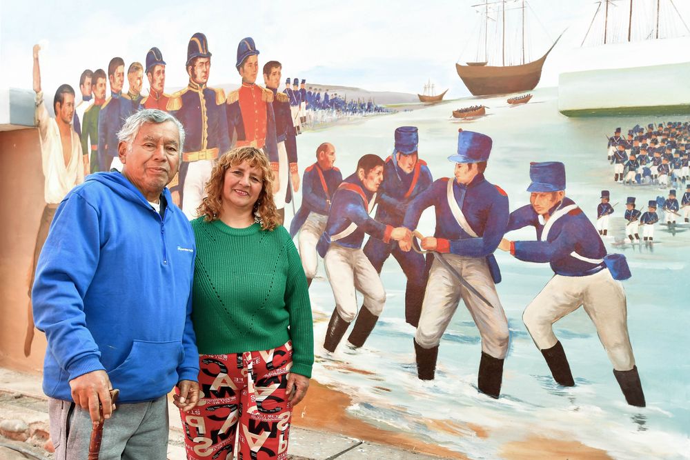 Los autores del mural, Enrique Muñante y su hija Nélida Muñante, artistas peruanos. Atrás, escena del desembarco del Ejército libertador en Para (Perú), en 1820. 