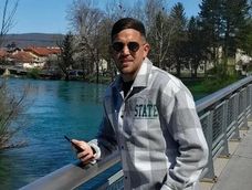 Una postal de Juan en Bosnia y Herzegovina. Detrás de él se observa vegetación abundante y relieve montañoso suave.