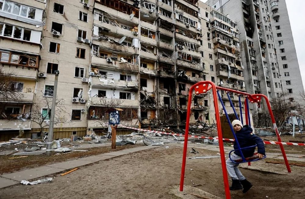 Un nene se sienta en un columpio frente a un edificio residencial dañado en Kiev, Ucrania, este viernes 25 de febrero de 2022. (Gentileza)