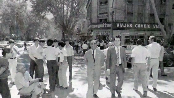 En la fotografía del Archivo General de la Provincia, se destaca una muy triste. Era el medio día del 2 de Abril de 1982. Autoridades militares y el gobernador de facto Bonifacio Cejuela caminan por Avenida San Martín, detrás cientos de mendocinos intentan comprar dólares. Foto: Orlando Pelichotti / Los Andes