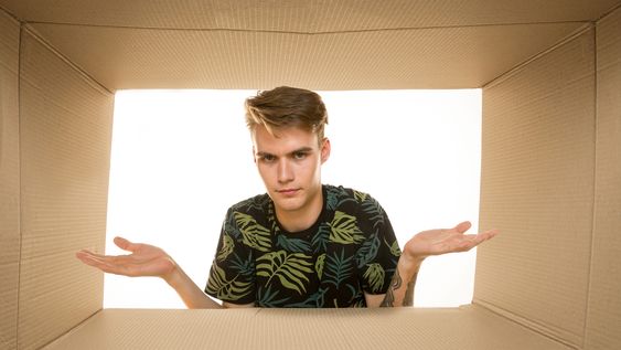 Un joven mira el interior de una caja y descubre que está vacía o que no hay nada. Foto: Freepik.