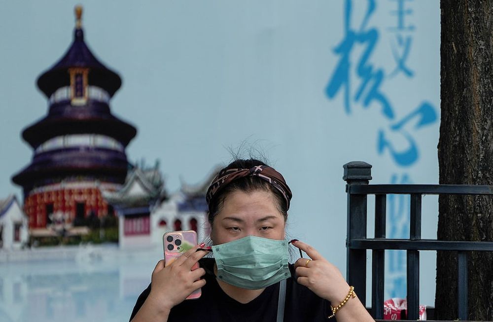 Una mujer se pone la mascarilla frente a un cartel. (AP)