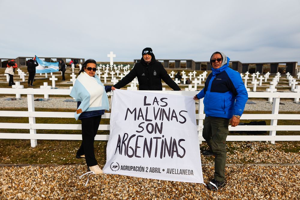 Excombatientes y familiares de caídos en la guerra de Malvinas sostienen una bandera con la frase "Las Malvinas son Argentinas" frente al cementerio de Darwin.