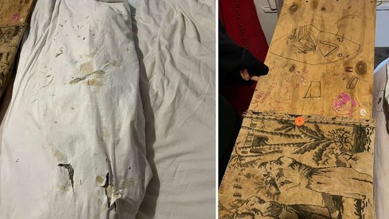 Sábanas manchadas y una tabla de madera, con dibujos y garabatos, colocada en la punta de la cama.