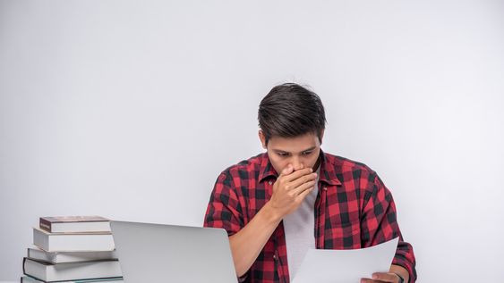 Un joven estudia mucho frente a su pila de libros y su computadora. En expresión común, se quema las pestañas estudiando.