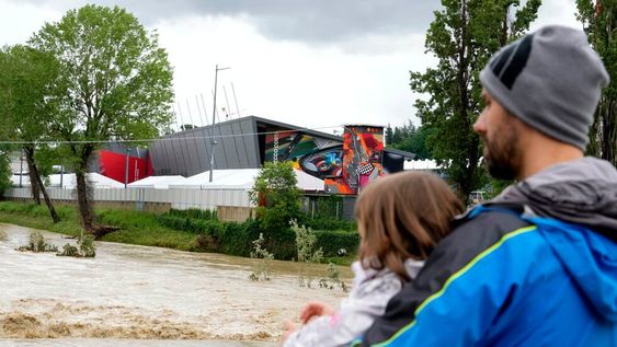 Un hombre con un niño en brazos contempla la crecida del río Santerno, y en el fondo de ve el circuito Enzo e Dino Ferrari en Imola, Italia, 17 de mayo de 2023. Las inundaciones obligaron a cancelar el GP Fórmula 1 de la Emilia Romagna. / AP