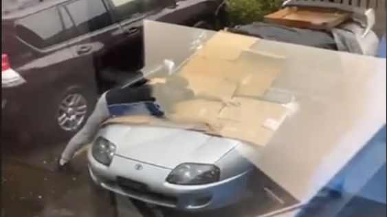 Al hombre se lo ve en el estacionamiento con su deportivo cubierto por cartones y abalanzándose arriba del vehículo tratando de cubrirlo de la lluvia con piedra. / Foto: Captura de video.