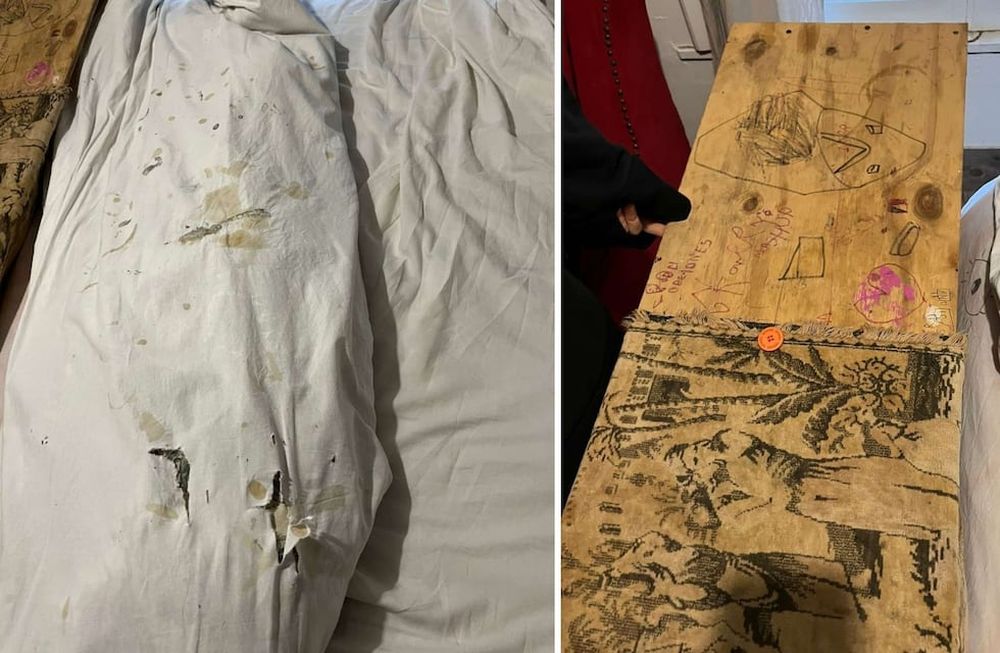 Sábanas manchadas y una tabla de madera, con dibujos y garabatos, colocada en la punta de la cama.