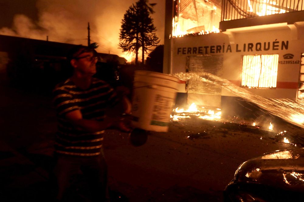 Una persona intenta controlar el fuego en su vivienda ocasionado por los incendios forestales durante la madrugada de este domingo, en Penco (Chile). 