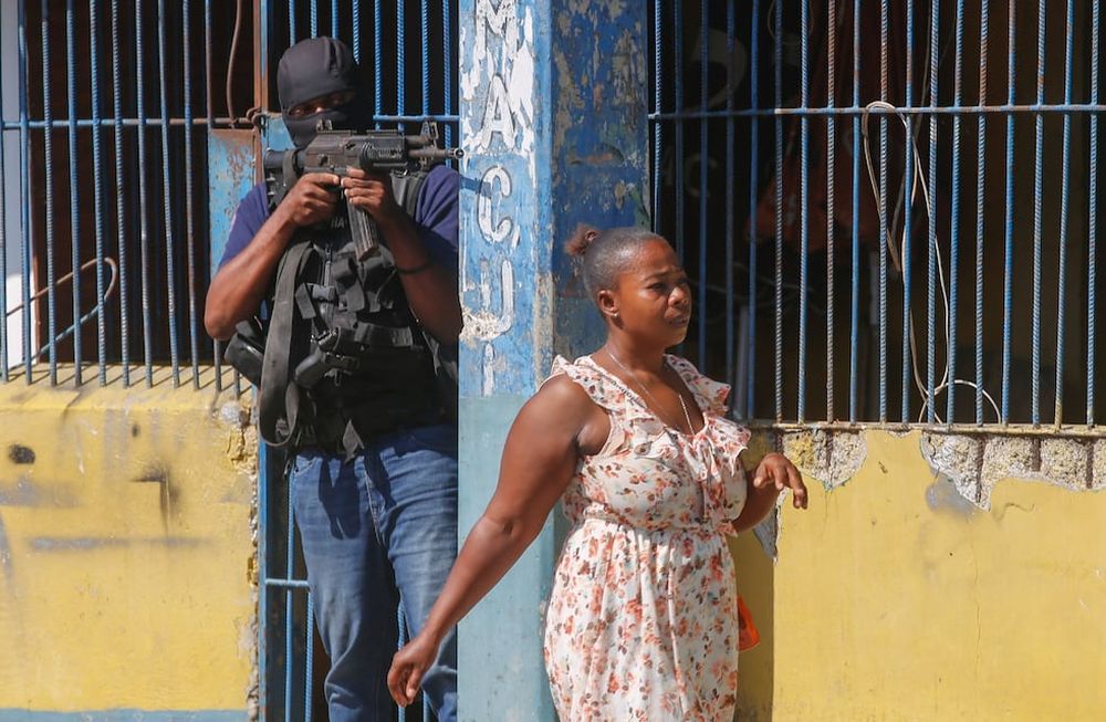 Una mujer pasa junto a un oficial de la Policía Nacional de Haití que custodia la Penitenciaría Nacional, en el centro de Puerto Príncipe, el jueves 14 de marzo de 2024. (Foto AP/Odelyn Joseph)