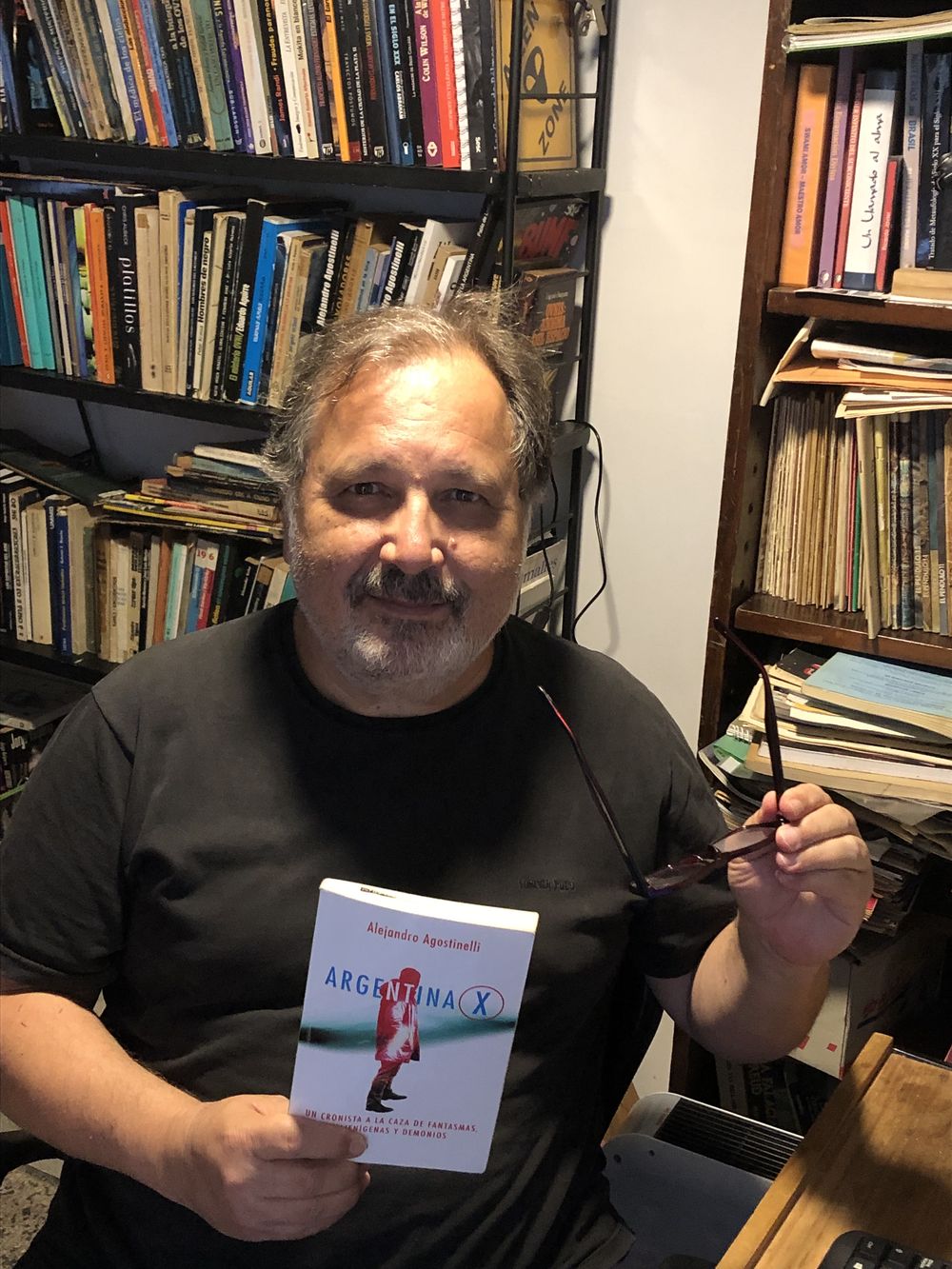 Alejandro Agostinelli en su lugar de escritura, con un ejemplar de su último libro: Argentina X.