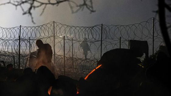 Un guardia fronterizo polaco patrulla cerca de una cerca de alambre de púas mientras los migrantes se calientan cerca de la fogata en la frontera entre Bielorrusia y Polonia cerca de Grodno. (AP)