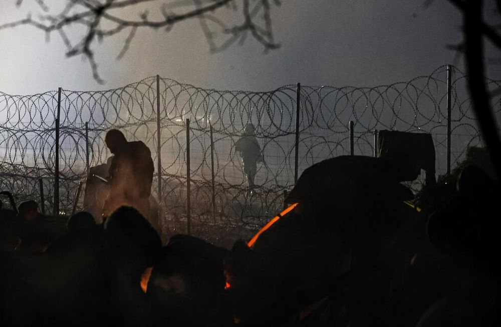 Un guardia fronterizo polaco patrulla cerca de una cerca de alambre de púas mientras los migrantes se calientan cerca de la fogata en la frontera entre Bielorrusia y Polonia cerca de Grodno. (AP)