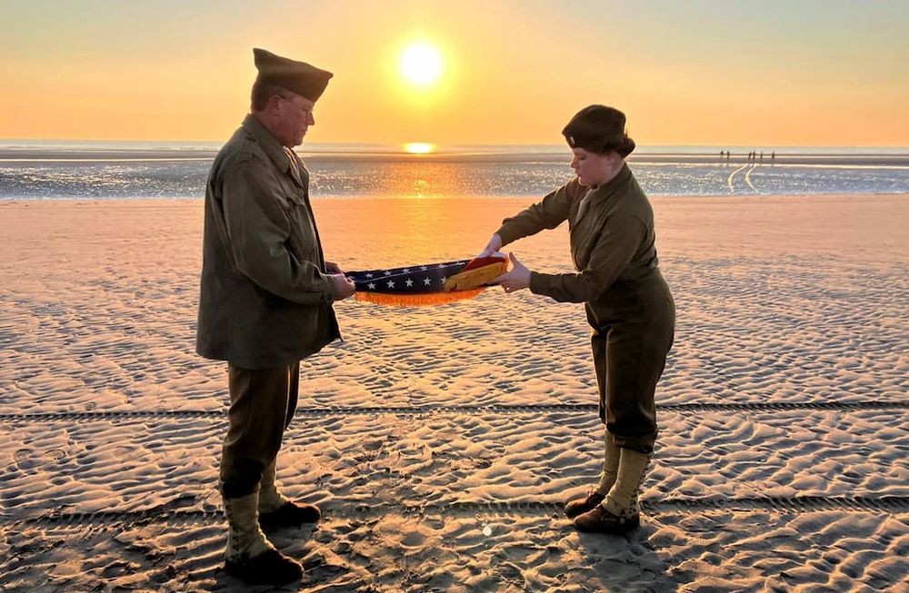 Christophe Receveur y su hija Julie, de Francia, extienden una bandera estadounidense que él compró hace seis meses en Gettysburg, Pensilvania, para conmemorar el Día D, el jueves 6 de junio de 2024 en la playa Utah, Normandía. (AP Foto/John Leicester)