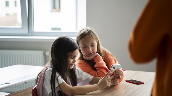 Dos alumnas miran su celular en lugar de atender la lección de la docente. Imagen ilustrativa de Freepik.