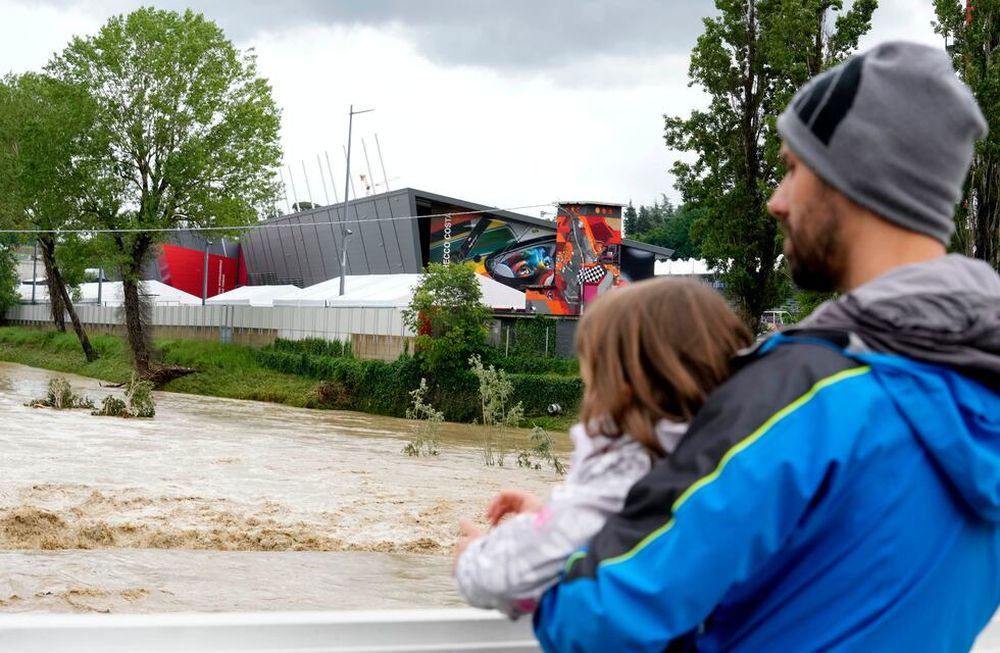 Un hombre con un niño en brazos contempla la crecida del río Santerno, y en el fondo de ve el circuito Enzo e Dino Ferrari en Imola, Italia, 17 de mayo de 2023. Las inundaciones obligaron a cancelar el GP Fórmula 1 de la Emilia Romagna. / AP