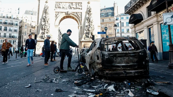 La gente pasa junto a un coche calcinado tras los enfrentamientos entre la policía antidisturbios y los manifestantes en París, Francia.