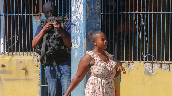 Una mujer pasa junto a un oficial de la Policía Nacional de Haití que custodia la Penitenciaría Nacional, en el centro de Puerto Príncipe, el jueves 14 de marzo de 2024. (Foto AP/Odelyn Joseph)
