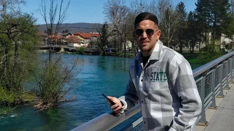 Una postal de Juan en Bosnia y Herzegovina. Detrás de él se observa vegetación abundante y relieve montañoso suave.