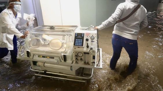 Enfermeras y médicas trasladan incubadoras para que las leven a un hospital seguro, ya que las inundaciones han afectado el servicio eléctrico.