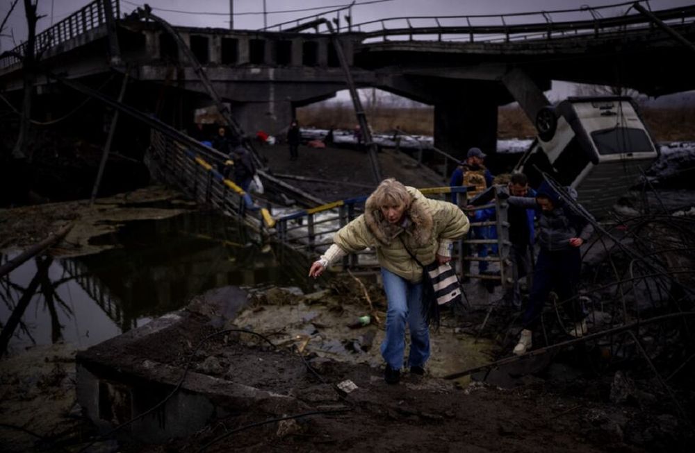 Una mujer corre mientras huye con su familia a través de un puente destruido en las afueras de Kiev, Ucrania.