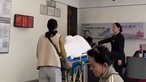 La mujer tuvo que llevar a su abuelo en camilla hasta el banco / Captura de vido