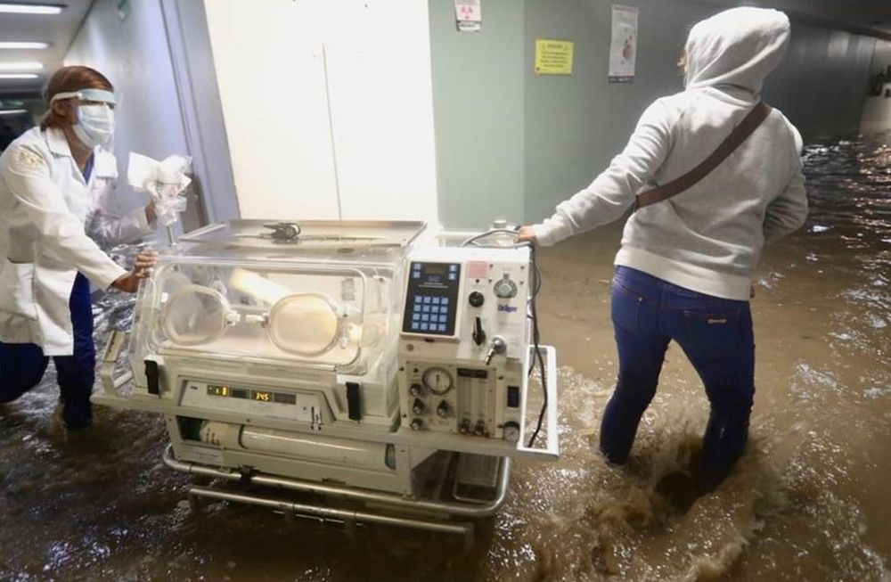 Enfermeras y médicas trasladan incubadoras para que las leven a un hospital seguro, ya que las inundaciones han afectado el servicio eléctrico.