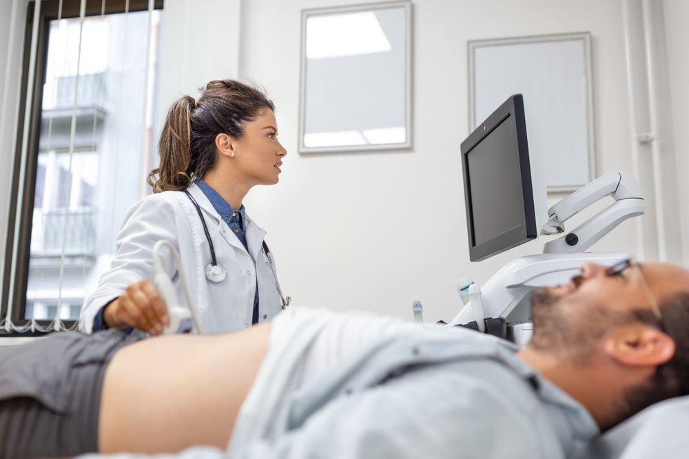doctora-cuidadosa-con-bata-blanca-sentada-frente-un-aparato-de-ultrasonido-y-realizando-diagnosticos-abdominales-con-transductor