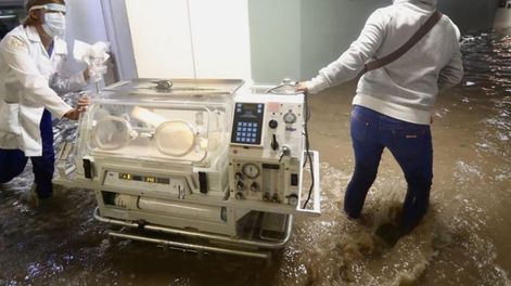 Enfermeras y médicas trasladan incubadoras para que las leven a un hospital seguro, ya que las inundaciones han afectado el servicio eléctrico.
