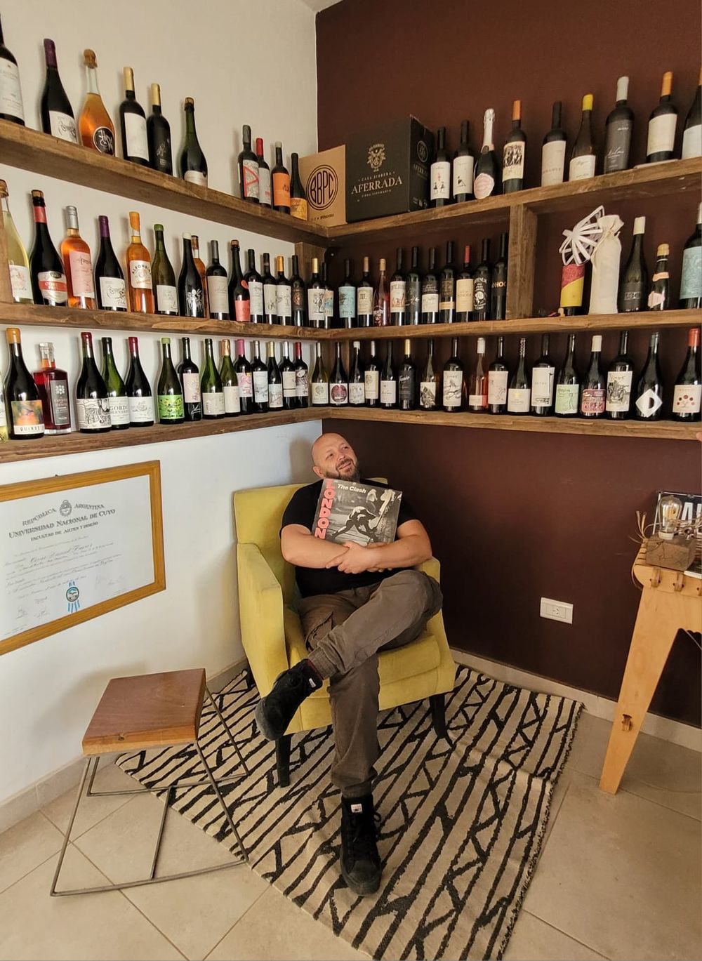 En un rincón de su estudio en La Consulta, Daniel posa rodeado de botellas que en la etiqueta llevan su autoría, sosteniendo un disco de The Clash y junto su título de la UNCuyo.
