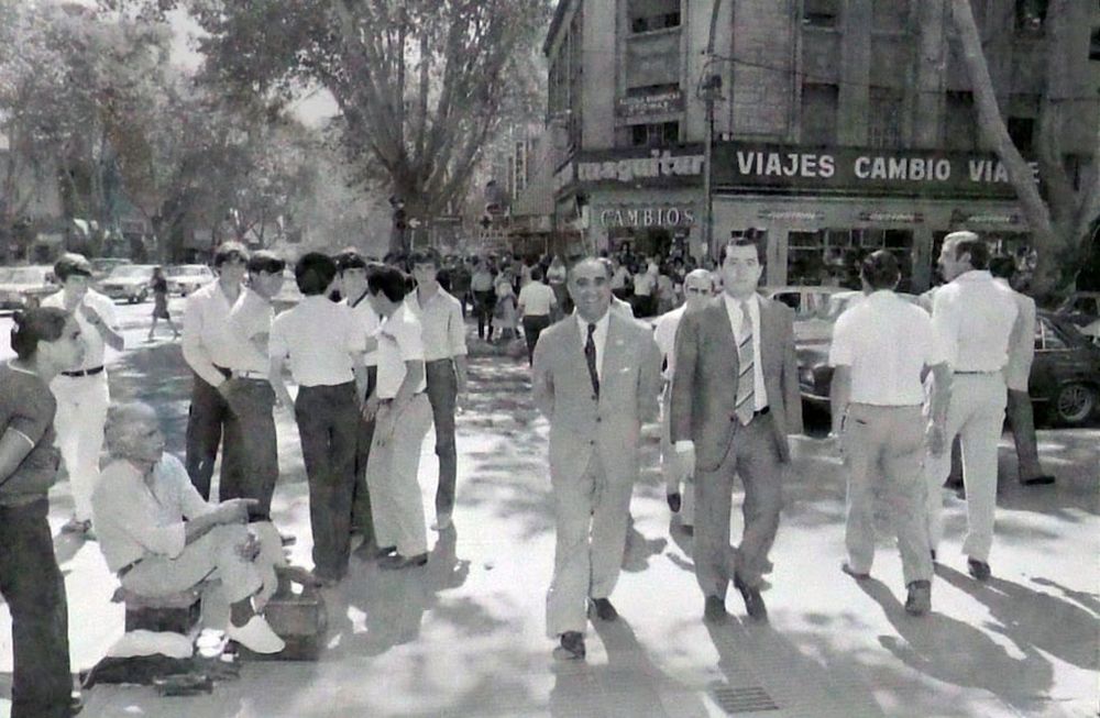 En la fotografía del Archivo General de la Provincia, se destaca una muy triste. Era el medio día del 2 de Abril de 1982. Autoridades militares y el gobernador de facto Bonifacio Cejuela caminan por Avenida San Martín, detrás cientos de mendocinos intentan comprar dólares. Foto: Orlando Pelichotti / Los Andes